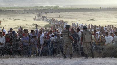 turkish soldiers stand guard syrian refugees wait behind border fences