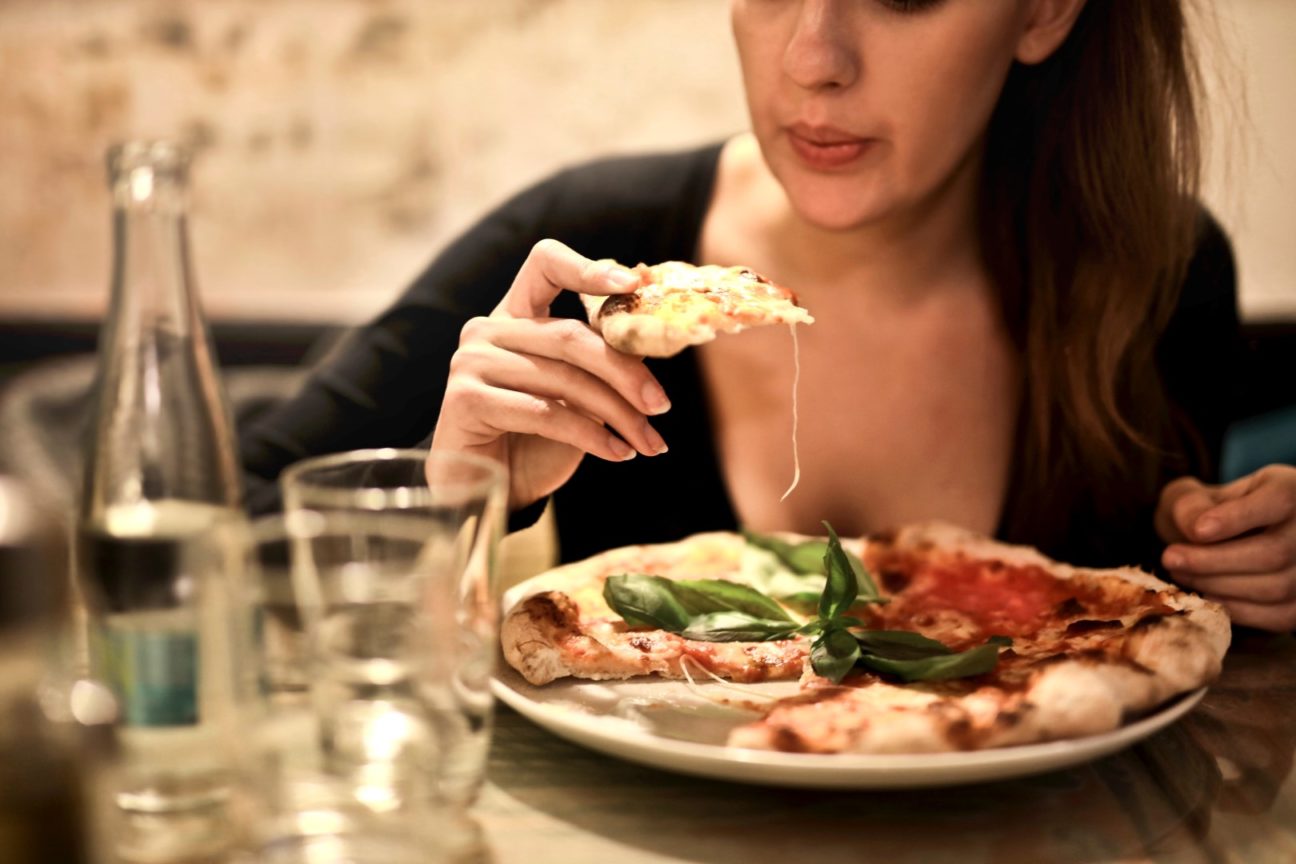 woman holds sliced pizza seats by table with glass 723031