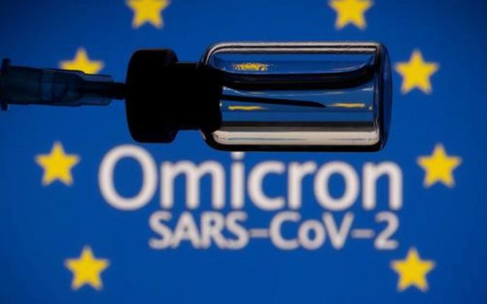 A vial and a syringe are seen in front of a displayed EU flag and words Omicron