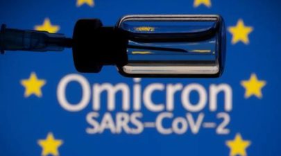 A vial and a syringe are seen in front of a displayed EU flag and words Omicron